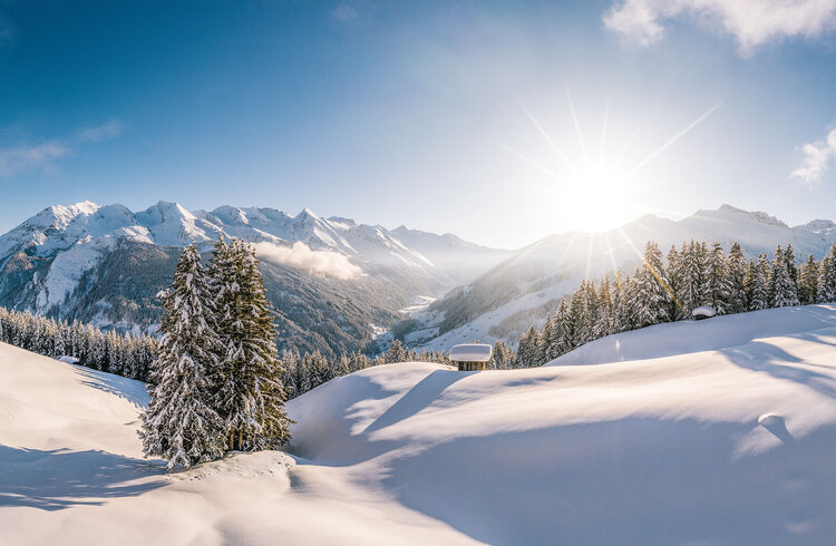 Eine atemberaubende Winterlandschaft mit schneebedeckten Bergen und strahlender Sonne, die über die Hügel scheint.
