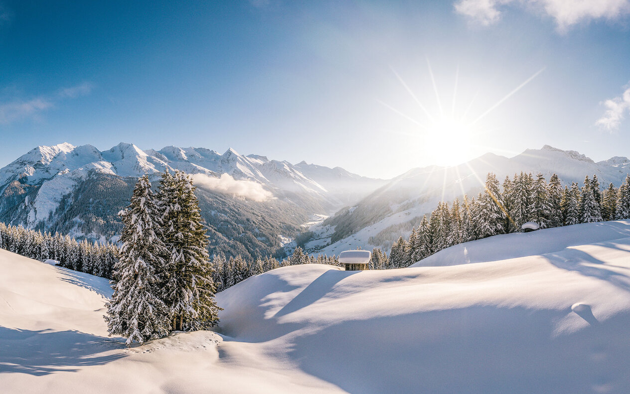 Eine atemberaubende Winterlandschaft mit schneebedeckten Bergen und strahlender Sonne, die über die Hügel scheint.