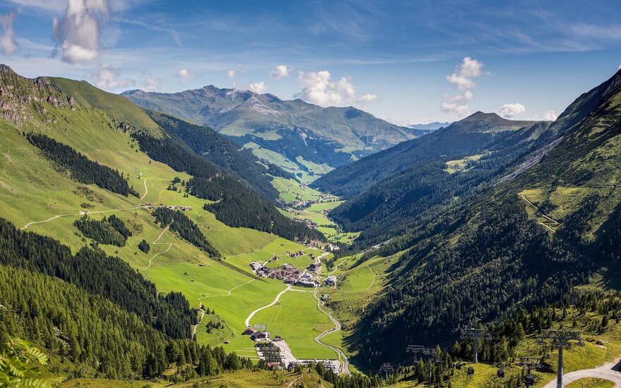Eine atemberaubende Berglandschaft mit grünen Wiesen und bewaldeten Hängen, die sich bis zu den Gipfeln erstrecken.