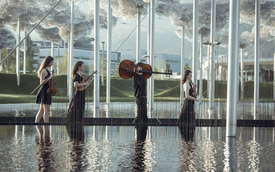 Vier Musikerinnen und ein Musiker stehen auf einer Plattform im Wasser, umgeben von reflektierenden Stäben und Wolken aus Kristallen.