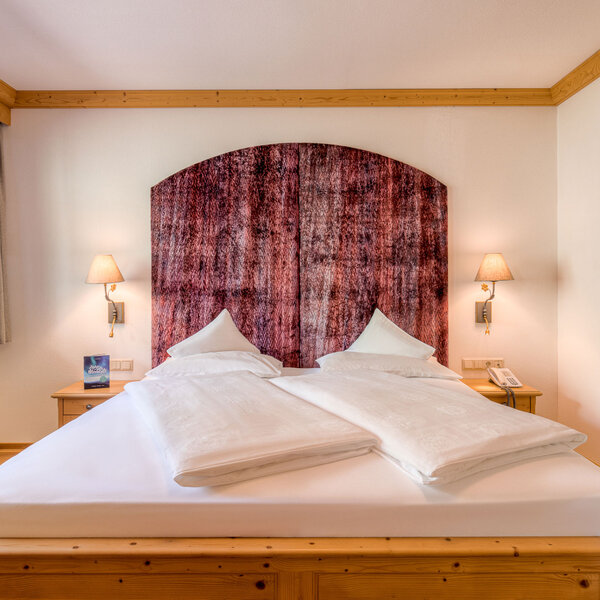 Ein gemütliches Schlafzimmer mit einem großen Doppelbett, das von einer eleganten, gemusterten Wandverkleidung umgeben ist.