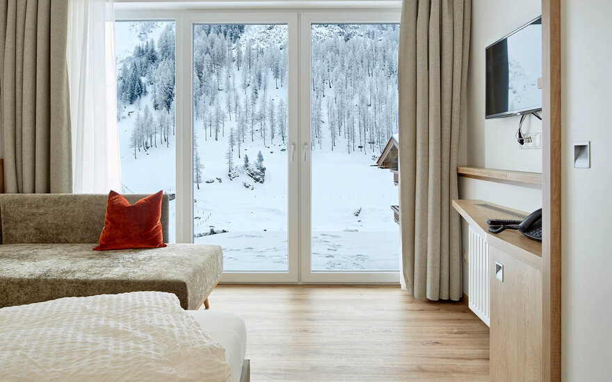 Ein einladendes Zimmer mit einem hellen Holzfußboden, einem Fernseher und einem Blick auf die verschneite Natur draußen.