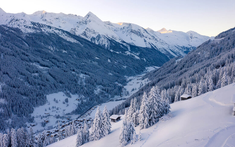 Eine verschneite Berglandschaft mit schneebedeckten Bäumen und einem kleinen Dorf im Tal, umgeben von majestätischen Gipfeln.