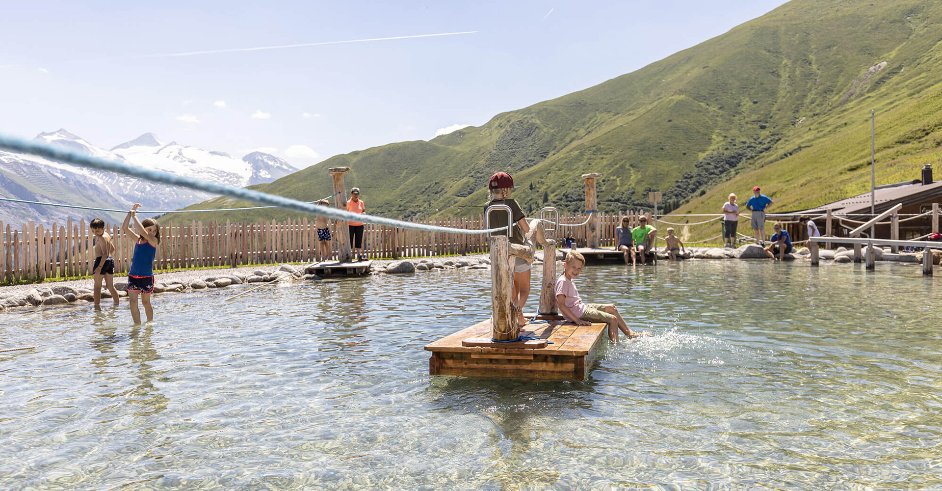 Kinder spielen fröhlich im Wasser, während die Berge im Hintergrund eine malerische Kulisse bieten.