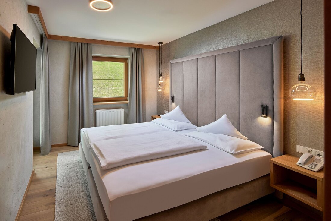 Ein modernes Schlafzimmer mit einem großen Doppelbett, sanften Farben und einem Fenster, das auf eine grüne Wiese blickt.