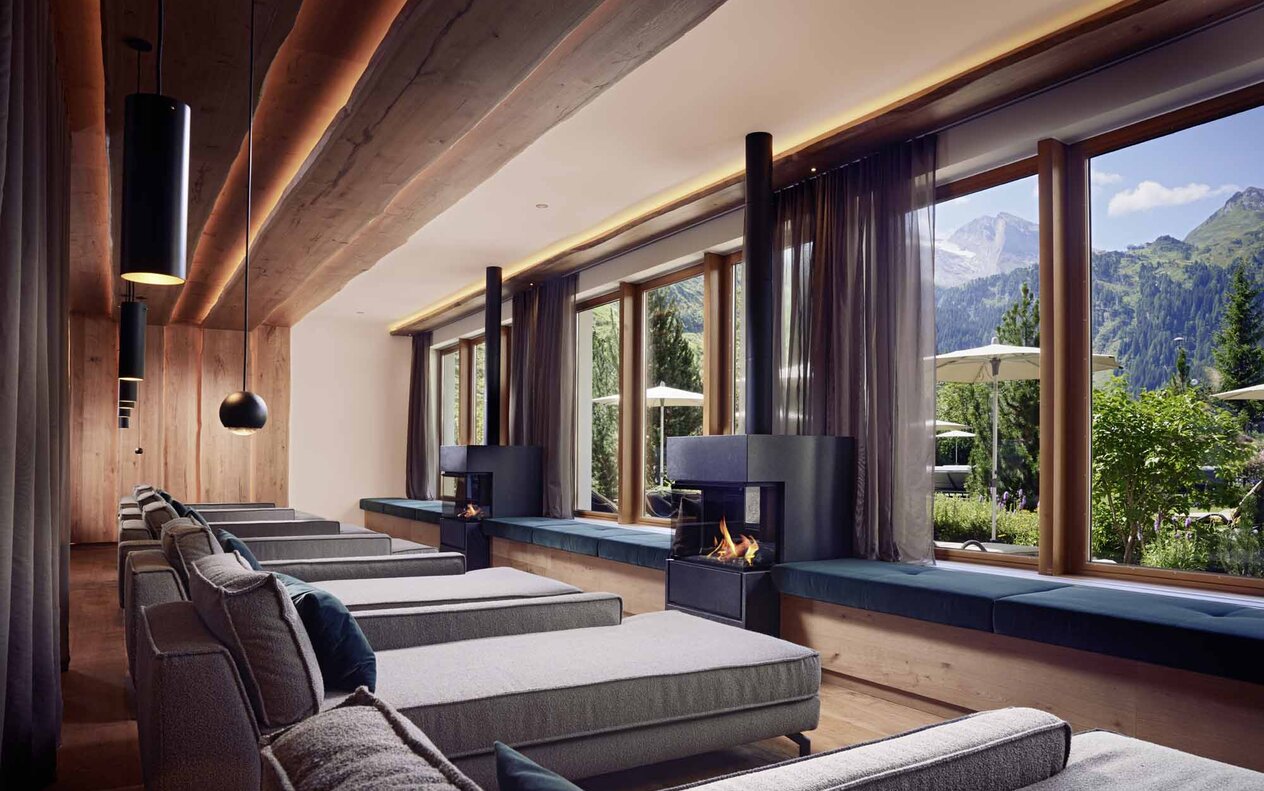 Ein eleganter Ruheraum mit gemütlichen Liegen, großen Fenstern und Blick auf die Berge und die Natur draußen.